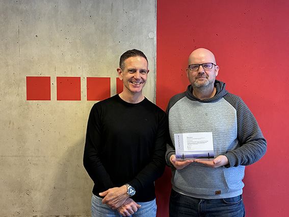 Steffen Maltusch steht freudestrahlend im Besprechungsraum von Fischer Planen und Bauen und hat die Auszeichnung Crestcom Leader Expert Levels Programm entgegengenommen.